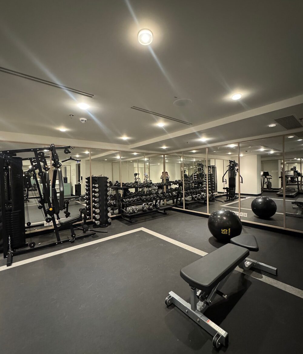 a photo of a gym with equipment that includes free weights, kettlebells, a workout bench, a giant exercise ball and all-in-one full-body workout machine.