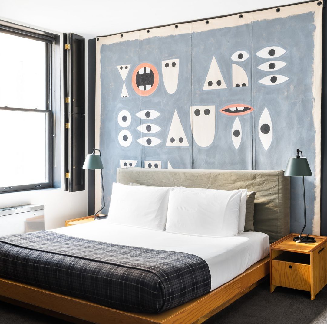 A bed is drenched in natural light flooding in from a window with stylish black, wooden indoor shutters
